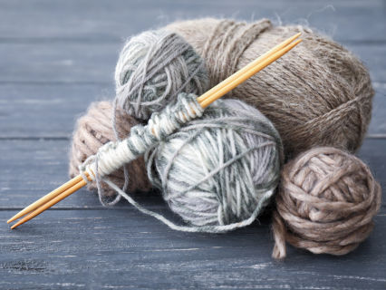 Wolle und Nadelsortiment Verschieden farbige Wollknäule mit zwei Stricknadeln aus hellem Holz, liegen auf einer dunkelgrauen Holzoberfläche