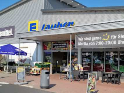 Edeka Markt Lauber Frontale Aufnahme vom Ladengeschäft Edeka Lauber in Meerholz. Eingangsbereich mit großem Öffnungszeitenbanner. Tisch- und Stuhlbestand von der innenliegenden Marktbäckerei. Aufbauten von Obst- und Gemüse, sowie Planzen- und Blumen.